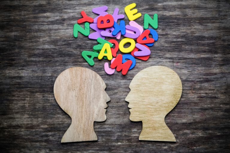 Silhouette cutouts of two people talking with colorful letters jumbled between them